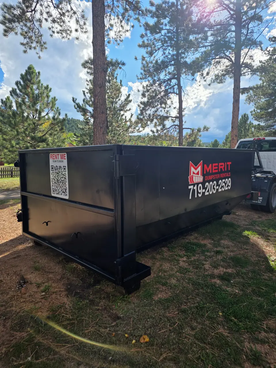 A Merit roll-off container on a residential lot with the scan-to-book code on the side